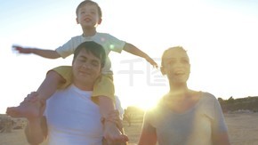 替身拍摄的一个年轻的家庭，走在沙滩上和谈话小男孩坐在父亲的肩膀上
