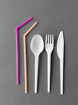 饮食，回收和生态学概念-白色一次性塑料叉子，刀和勺子用粉红色的稻草在灰色的背景上一次性塑料叉，刀，匙和吸管