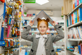小女小学生在文具店拿着在她的头的文件夹女童在商店里买办公用品，超市里的小学生