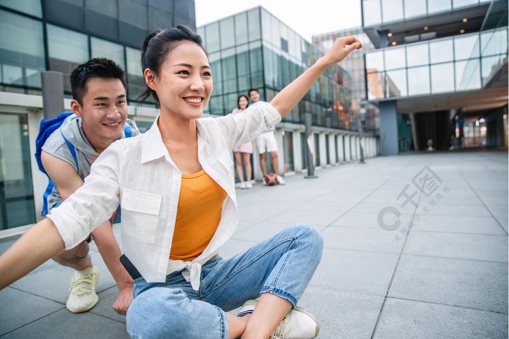 年轻男子向前推着坐在滑板上的女友