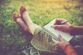女性的手，用笔在外面的草地上的笔记本上写