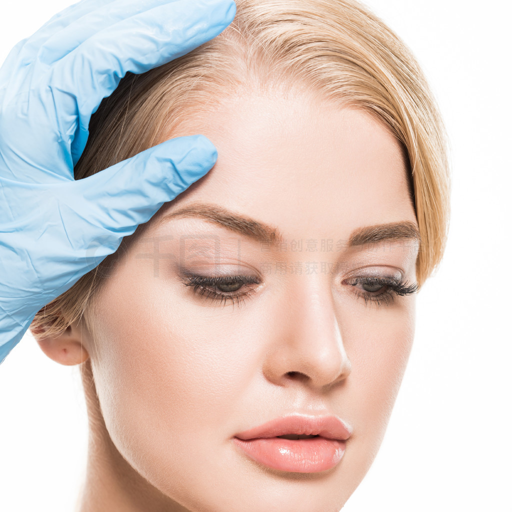 cropped shot of cosmetologist touching forehead of beautiful young woman isolated on white