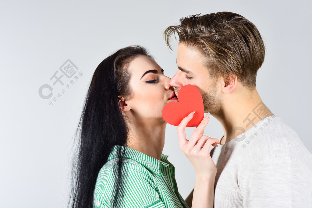 情侣在爱亲吻和隐藏的嘴唇背后的心卡庆祝情人节可爱夫妇的感性吻近在