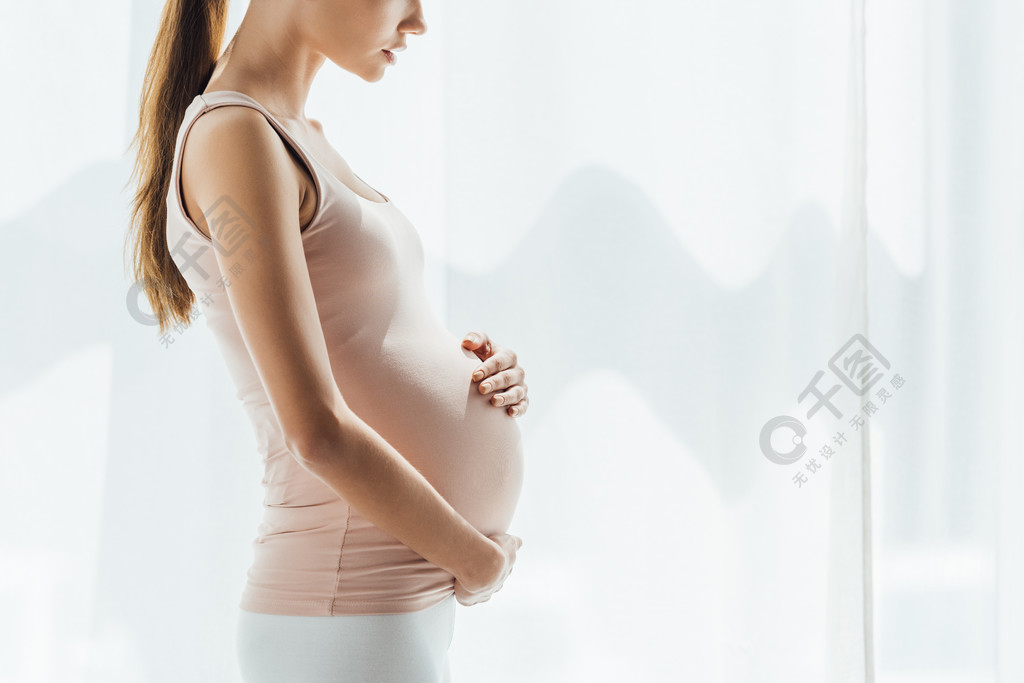 怀孕妇女在家中触摸腹部的裁剪视图