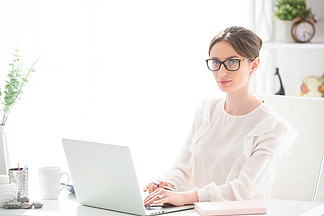 一个年轻的女人在办公桌前工作，办公室里有一台笔记本电脑。妇女事务，远程工作.