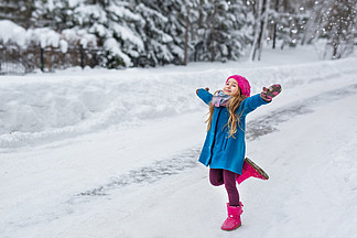 小女孩穿着一件蓝上衣和粉红<i>色</i>的帽子和靴子，到了冬季的森林里，伸出两臂运行