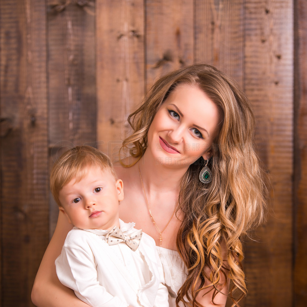 baby blond boy in a white suit white socks with his mother on a wooden background. next to a small d