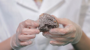 明亮的灰色红宝石水晶矿石在手与手套。结晶是实验室中固体形成的自然或人工过程.