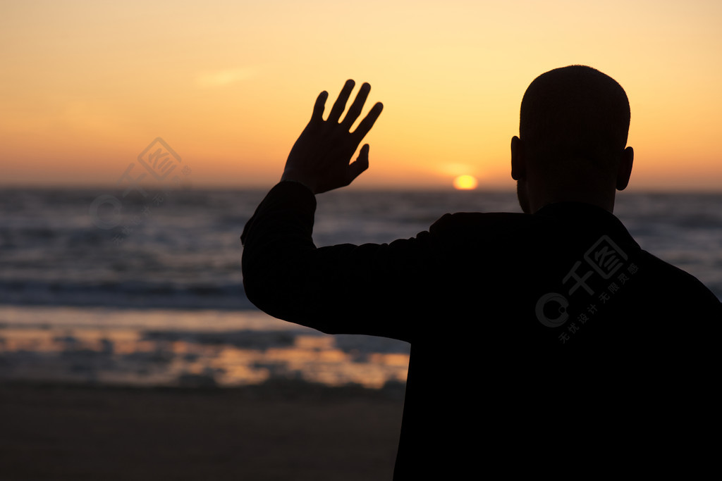 男性轮廓在日落在海滩上挥手致意