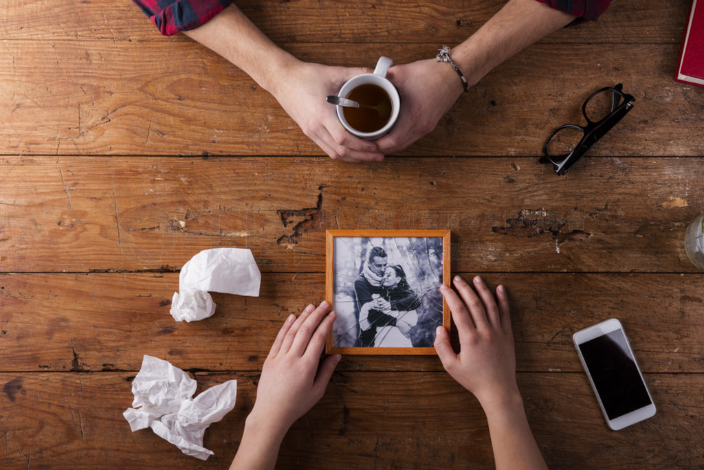 Sad mans, womans hands holding broken picture of romantic couple.