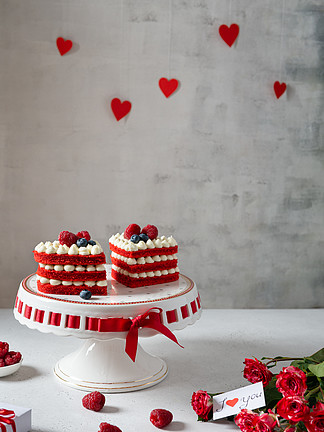 盘上有红绒心形蛋糕，背景上有红玫瑰。 情人节的概念。 <i>甜</i><i>蜜</i>的礼物 面包店、糖果店