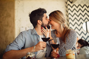 英俊的男子亲吻他的女朋友在鼻子。夫妇喝葡萄酒咖啡馆和庆祝情人节.