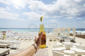 男性手捧着一瓶啤酒，在阳光明媚的天空和清澈的大海上。背景是一个美丽的海滩度假胜地。度假理念.