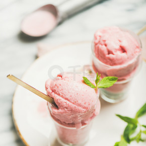 健康低卡路里的夏季甜点。自制草莓酸奶冰淇淋在玻璃上的新鲜薄荷在板上灰色大理石桌面背景.