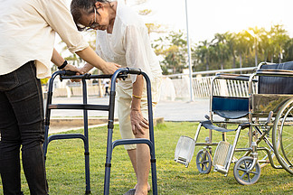 年长的亚洲女性病人在康复过程中，用手<i>触</i><i>摸</i>膝盖，关节受伤，骨头问题，膝盖疼痛，走路时使用步行机，老年妇女患有骨质疏松症、痛风、佝偻病