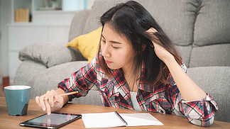亚裔女学生在家做作业，女性喝咖啡，用平板电脑在客厅的房间里找。生活方式 妇女放松在家里的概念.