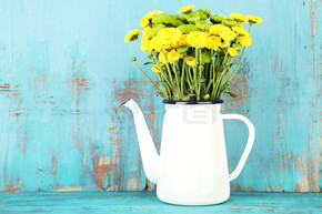 黄色和绿色花在装饰上色彩木制背景的茶壶