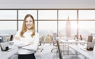 Smiling beautiful business lady with cross hands <i>is</i> standing in a modern panoramic office in New Yor