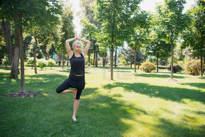 妇女在公园草在树姿势 (Vrksasana) 练习瑜伽
