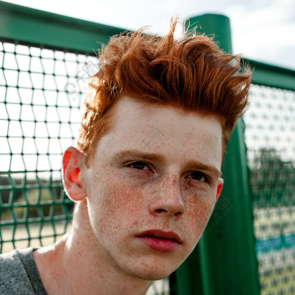一个年轻英俊红头发时尚的男孩在晴天室外站在体育场附近穿休闲服装