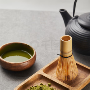 在红茶壶和茶碗旁的木板上选择性聚焦绿色火柴粉和竹须