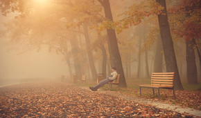 男人坐在一个大雾天公园的长凳上