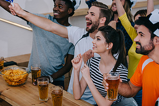 激动的多文化的小组朋友在足球帽子庆祝和看足球比赛在酒吧
