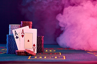 两个A，心脏和球杆，靠在彩色晶片堆在蓝色的桌子上。黑色，烟的背景，红色和蓝色的背光。赌场.