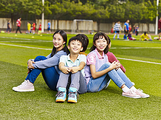 <i>群</i>快乐亚洲小学学生坐在草地上
