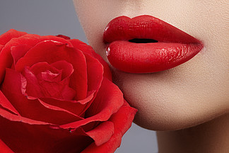 特写美丽的女性嘴<i>唇</i>与明亮的<i>唇</i>彩化妆。完美的清洁皮肤，性感的红<i>唇</i>化妆。与红色玫瑰花朵的美丽面貌画像。面貌和化妆品