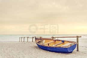 老黄蓝色木质小船在白色的沙滩上温暖日落大道上