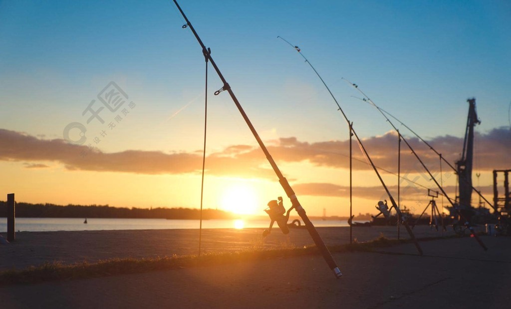 钓鱼竿，背景码头河岸上的旋转卷轴。日出。以湖为背景的
